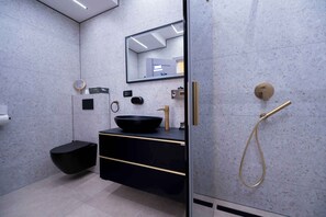 Un baño moderno con tocador negro, espejo redondo, cabezal de ducha dorado y lavabo negro.