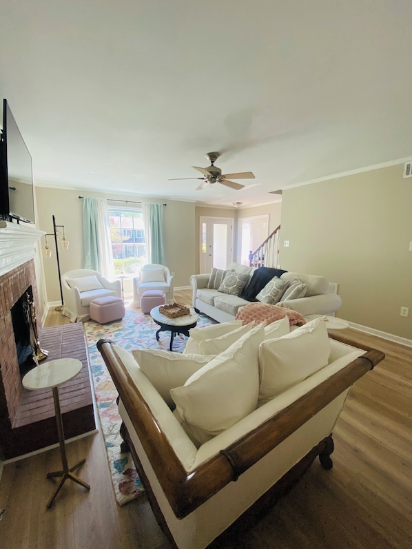 A living room with a fireplace, a ceiling fan, and a staircase leading to another level. - Masters 2026 (Martinez)