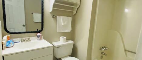 A bathroom with a toilet, sink, mirror, and shower.