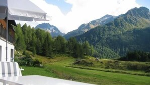 A white outdoor table with striped cushions, set against a backdrop of a mountainous landscape with dense forests and a clear sky. - La Solina Lunghin by Interhome (Maloja)