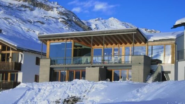 A modern chalet with large glass windows, a wooden balcony, and a snowy mountain backdrop. - La Solina Lunghin by Interhome (Maloja)
