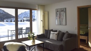 A cozy living room with a sofa, a small table with a plant, and a view of snowy mountains through large windows. - La Solina Lunghin by Interhome (Maloja)