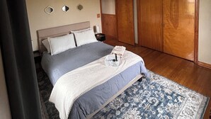 A bedroom with a bed, a nightstand, a wooden wardrobe, and a patterned rug.