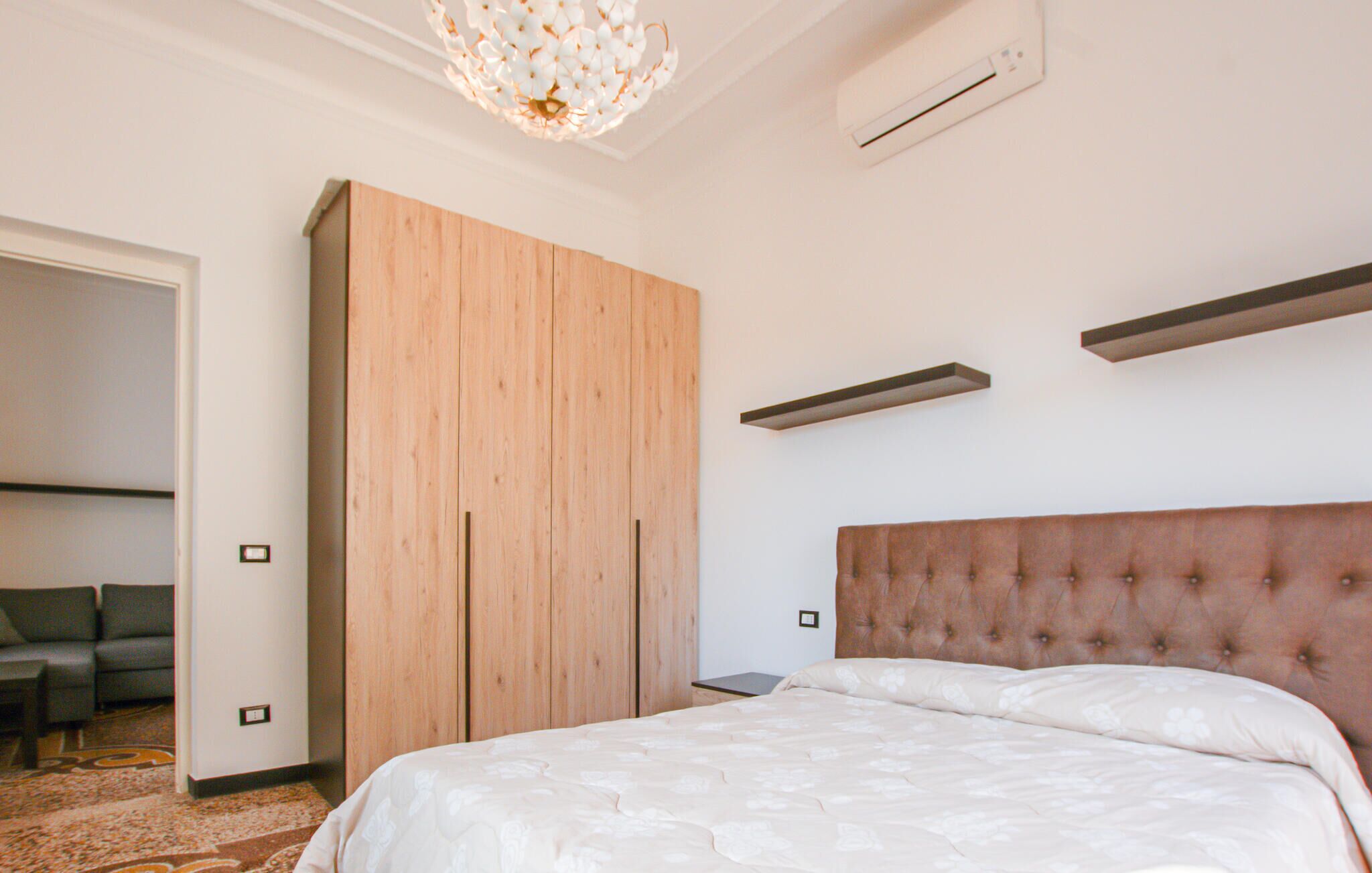 A bedroom with a bed, a wooden wardrobe, a hanging light fixture, and a wall-mounted air conditioner.