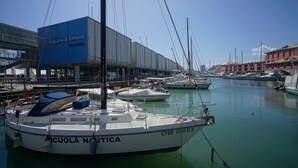Un port esportiu amb barques amarrades, un edifici amb la inscripció "Acquario di Genova Porto Antico" i un cel serè.