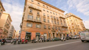 Un edifici de diversos pisos amb una filera de cotxes i patinets aparcats al carrer.