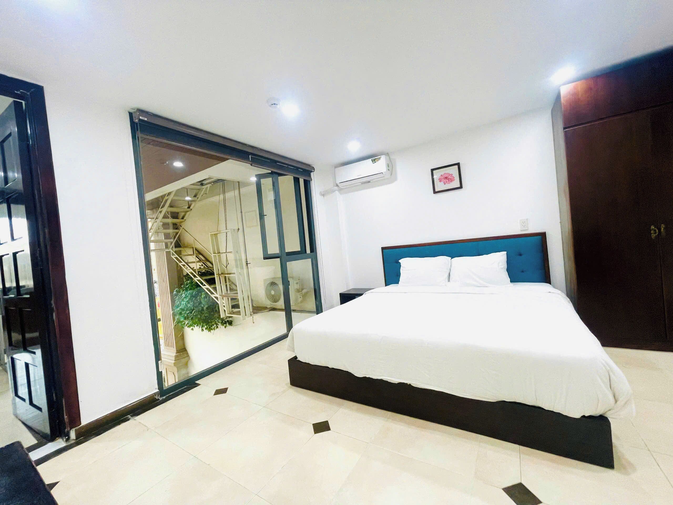 A bedroom with a bed, a sliding glass door leading to a balcony, a small plant, and a wall-mounted air conditioner.