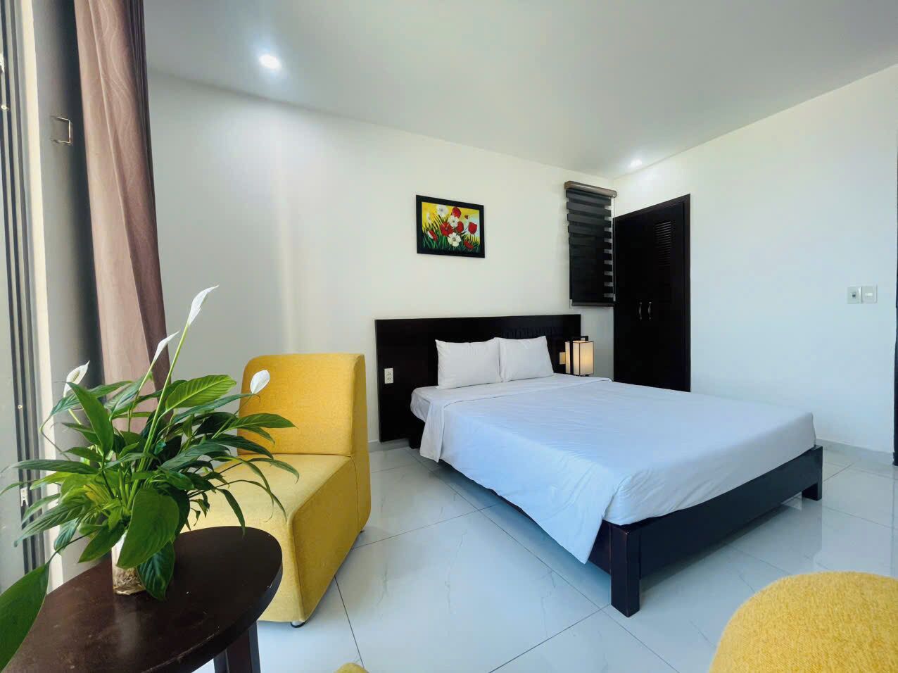 Habitación de hotel con una cama, una silla, una planta en maceta y un cuadro en la pared.