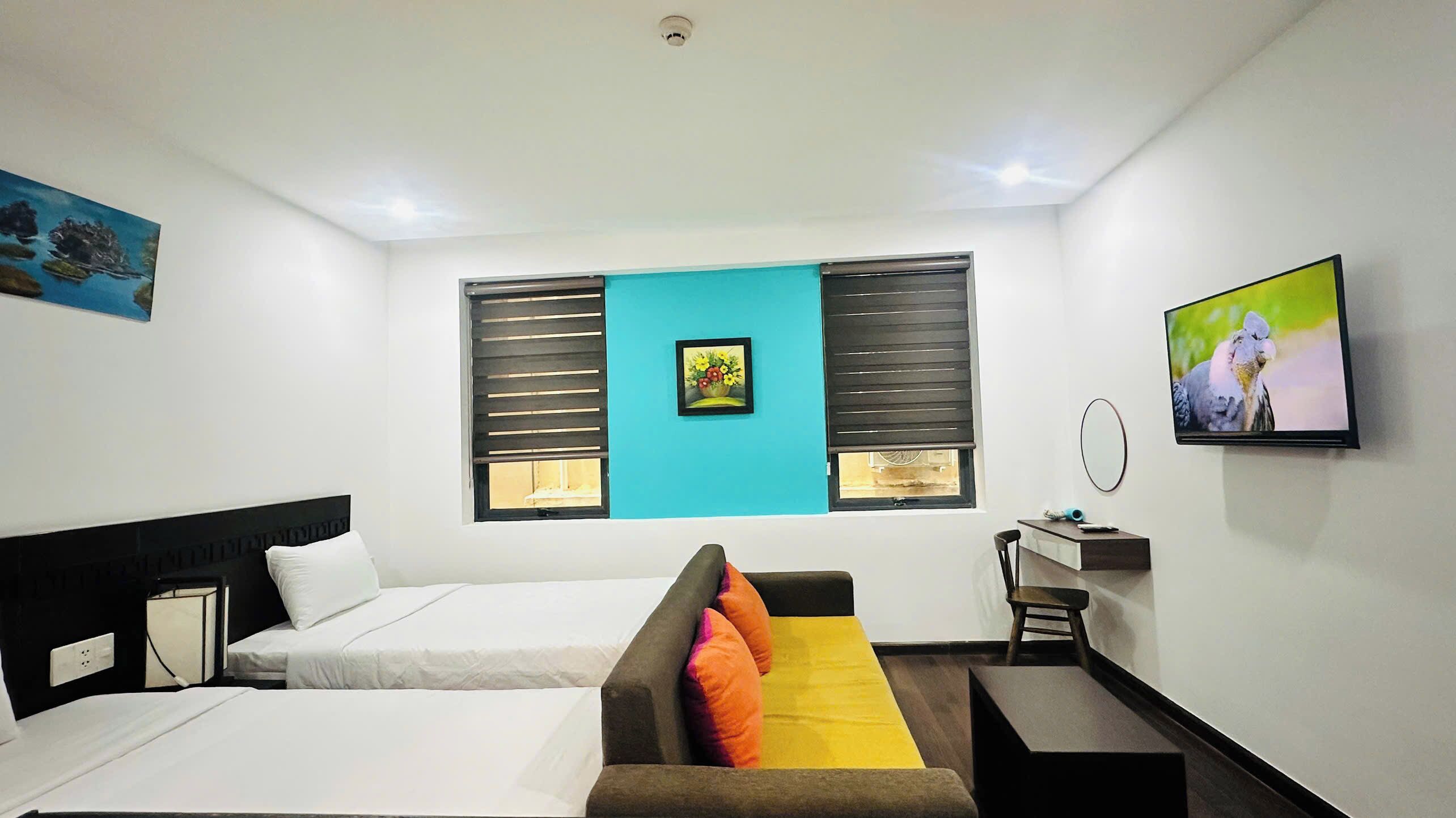 A hotel room with two beds, a desk, a chair, a TV, and a painting on the wall.