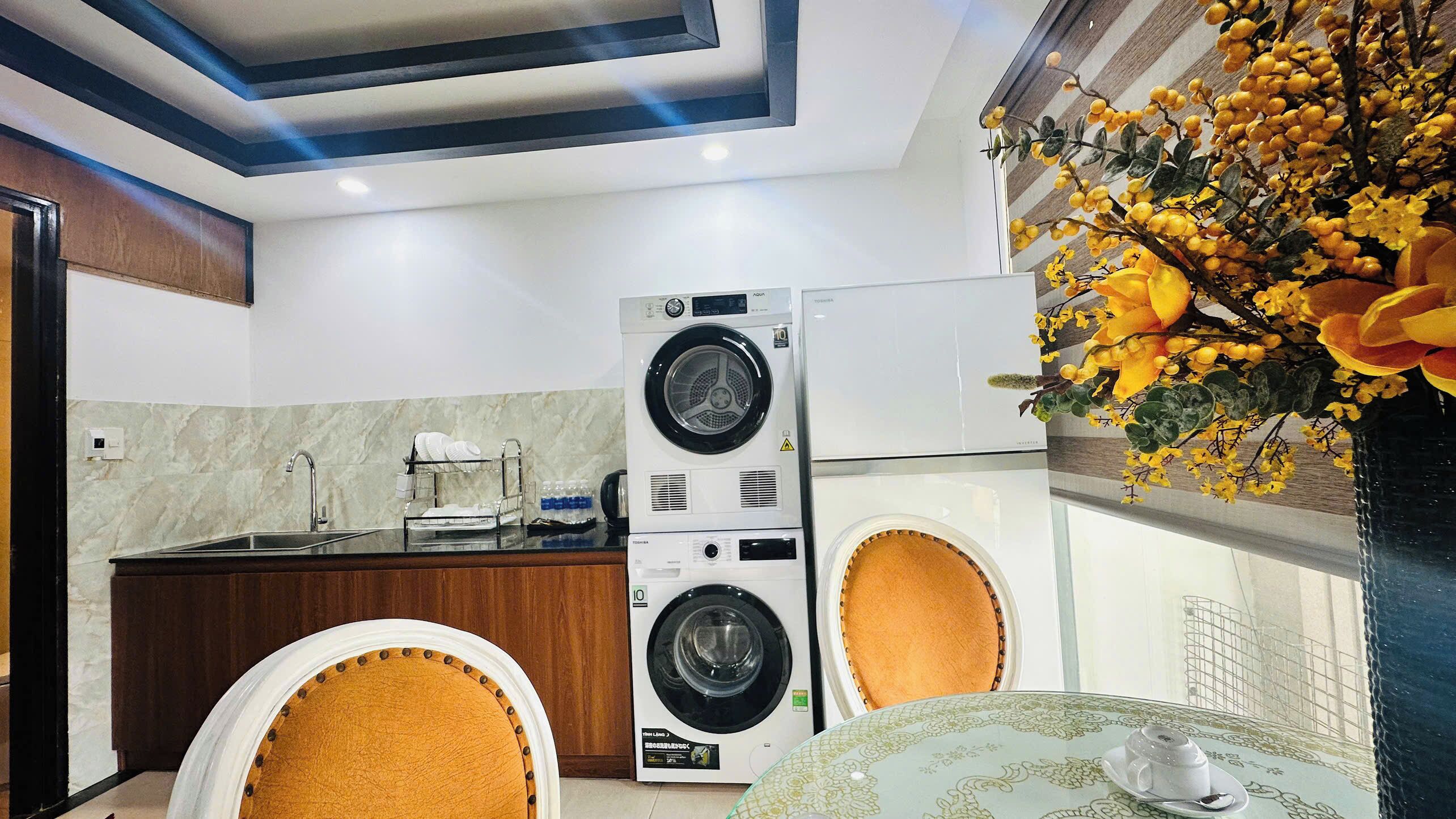 Una cocina compacta con lavadora incorporada, un comedor con mesa y sillas, y una planta decorativa.