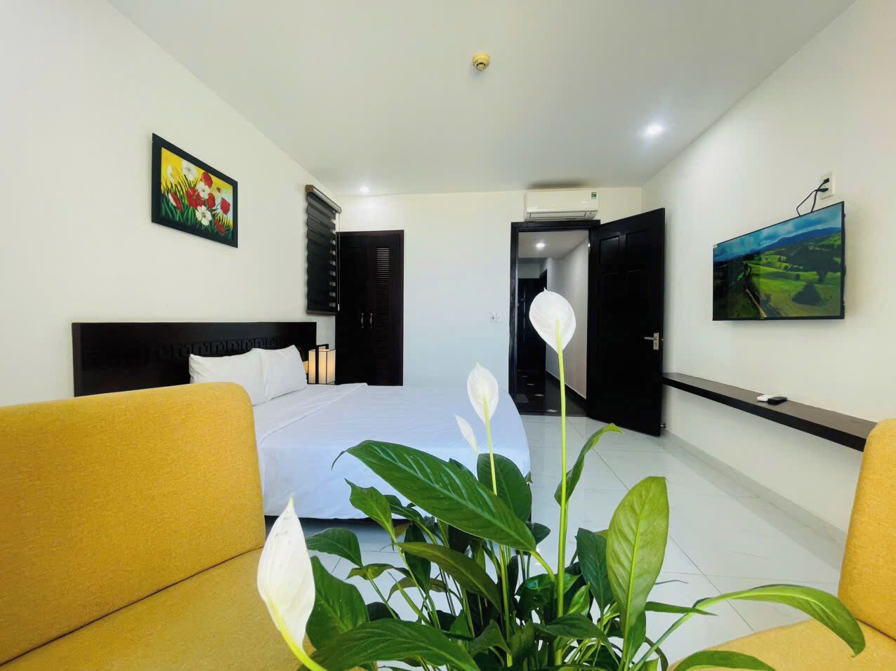 A modern hotel room with a bed, a sofa, a potted plant, and artwork on the walls.