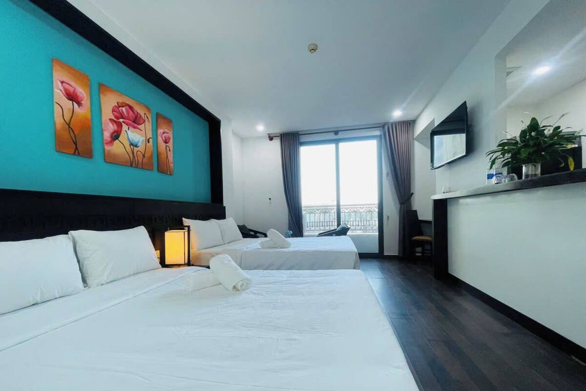 A hotel room with two beds, a desk, a TV, and a balcony view.