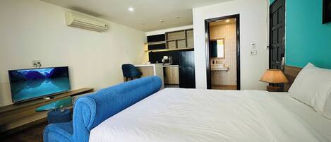 Una habitación de hotel con cama, televisión, escritorio y kitchenette.