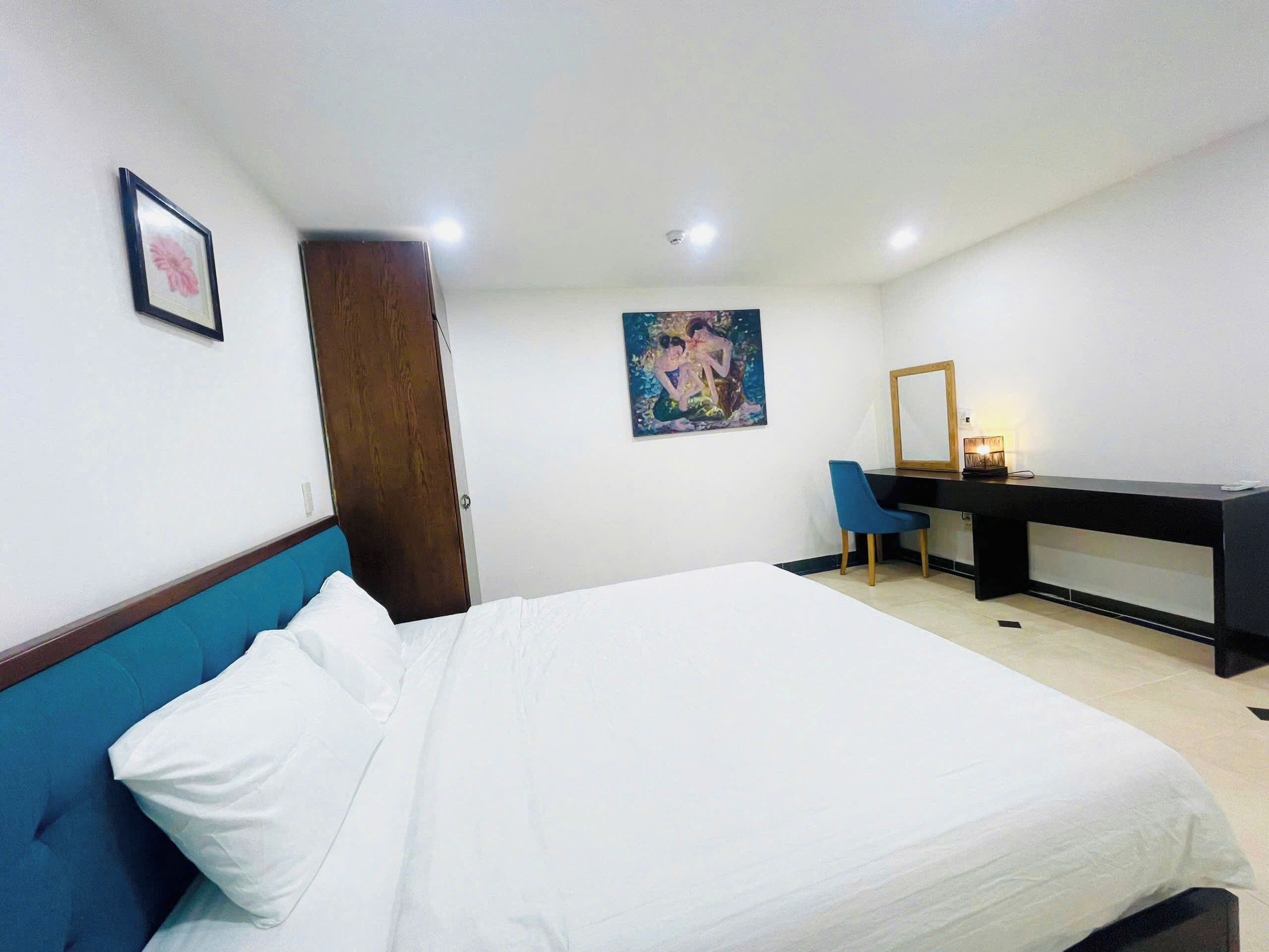 Habitación de hotel con una cama, un escritorio, una silla, una puerta y un cuadro en la pared.