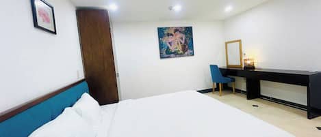 Habitación de hotel con una cama, un escritorio, una silla, una puerta y un cuadro en la pared.