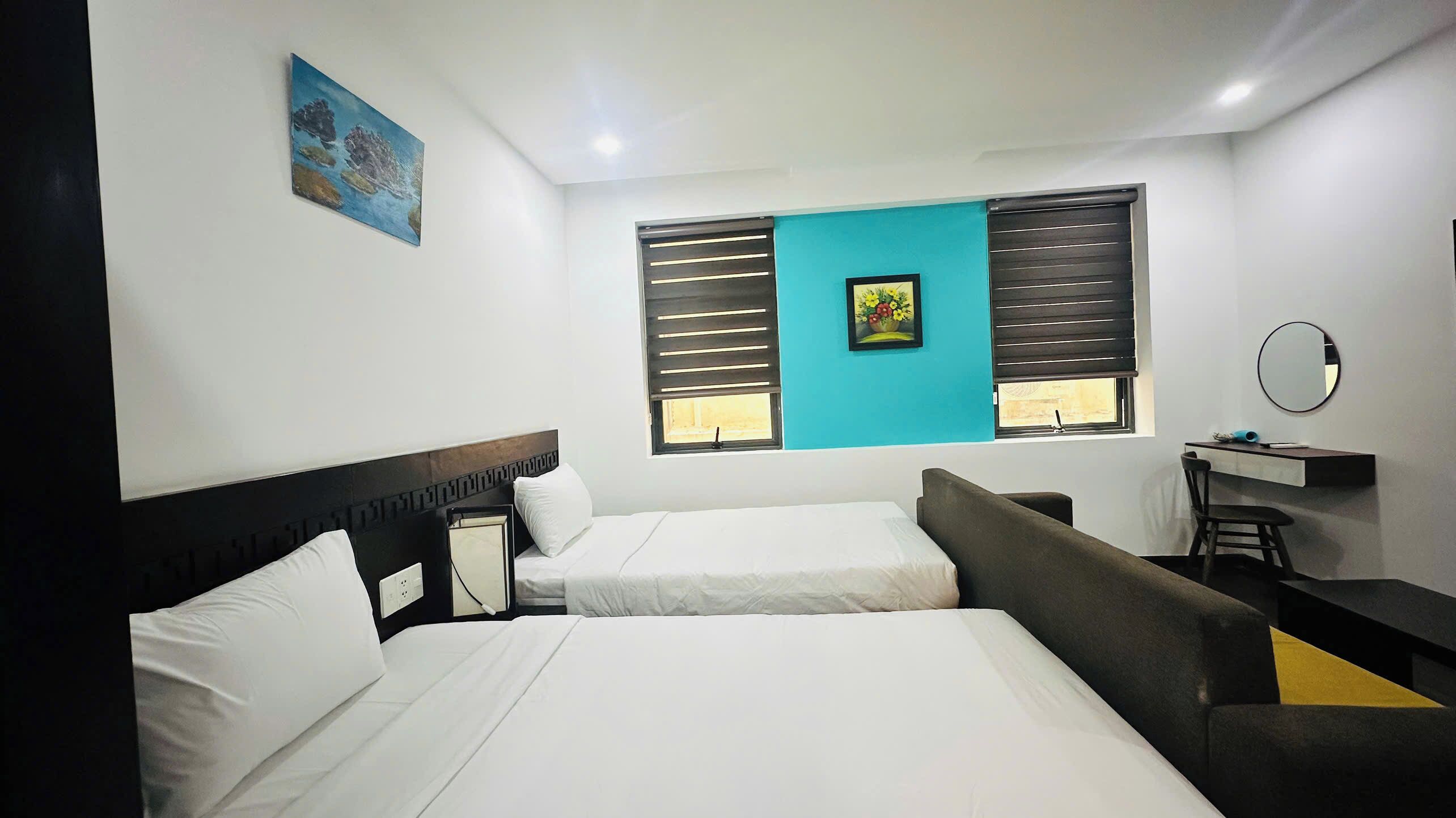 A hotel room with two beds, a desk with a chair, a small table, and a wall-mounted mirror.