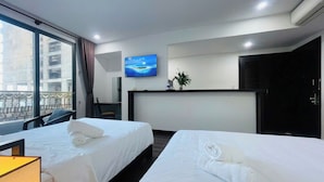 Une chambre d’hôtel avec deux lits, une télévision, un bureau et une fenêtre donnant sur des immeubles.