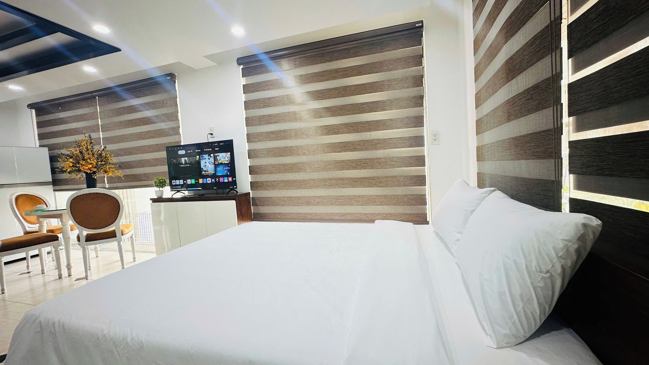A hotel room with a bed, a desk with a TV, a chair, and a wall with a striped pattern.