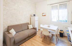 Ein gemütlicher Wohnraum mit Sofa, einem kleinen Tisch mit Stühlen, einem Kühlschrank und einem Fenster mit Jalousien.