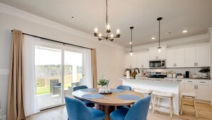 Een moderne keuken met witte kasten, een centraal eiland met krukken, en een eethoek met een ronde tafel en blauwe stoelen.