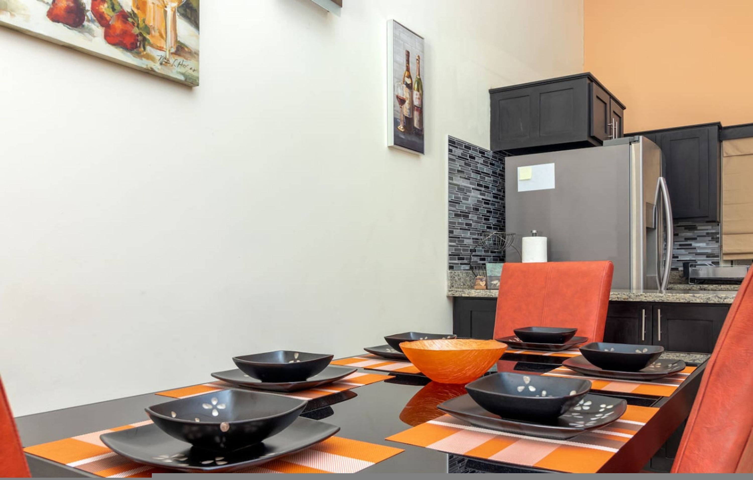 Ein Essbereich mit einem für vier Personen gedeckten Tisch, schwarzen Schüsseln, orangefarbenen Platzsets und einer großen orangefarbenen Schale als Mittelstück.