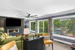 Een moderne woonkamer met een open haard, een plafondventilator en uitzicht op een meer.
