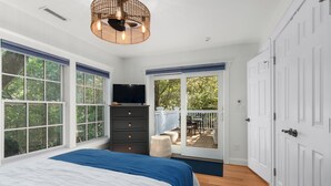 A bedroom with a bed, dresser, TV, and a sliding glass door to a balcony. - "Slow Your Roll" is a pet-friendly, five-bedroom, 4.5-bath Maritime Forest (Bald Head Island)