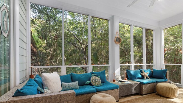 A sunroom with wicker furniture, large windows, and a view of trees. - "Slow Your Roll" is a pet-friendly, five-bedroom, 4.5-bath Maritime Forest (Bald Head Island)