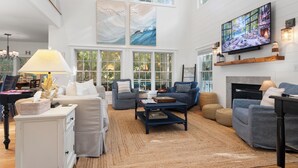 A spacious living room with a fireplace, large windows, and a flat-screen TV. - "Slow Your Roll" is a pet-friendly, five-bedroom, 4.5-bath Maritime Forest (Bald Head Island)