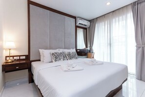 A hotel room with a large bed, a nightstand with a lamp, an air conditioning unit, and a window with curtains. - 1BR Poolside Fisherman Village C272 (Koh Samui)