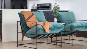 Een moderne woonkamer met een blauwgroene bank, een metalen frame en een keuken op de achtergrond.