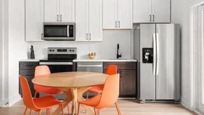 Eine moderne Küche mit weißen Schränken, einem Edelstahl-Kühlschrank, einer Mikrowelle und einem Esstisch mit orangefarbenen Stühlen.