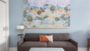 Ein Wohnzimmer mit einem braunen Sofa, einem Kissen, einem gerahmten Landschaftsbild und einer Stehlampe.