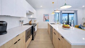 A modern kitchen with white cabinets, a black stove, and a large window with curtains. - Hyve-Anthem-Private Balconies-Walk to Broadway (Nashville)