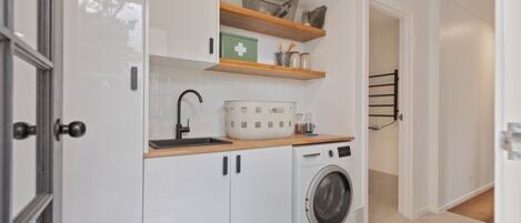 Una cocina funcional con lavadora, estantes de madera y un armario para medicamentos.