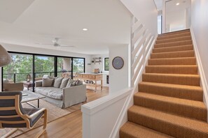 A modern interior with a staircase, a sofa, a dining area, and a view through large windows. - The Reid Residence - Merimbula (Merimbula)