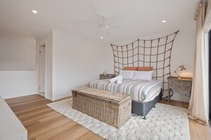 A bedroom with a bed, a nightstand, a lamp, a wicker chest, and a ceiling fan. - The Reid Residence - Merimbula (Merimbula)