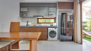 A modern kitchen with grey cabinets, a built-in microwave, a washing machine, and a dining area with a wooden table. - Sedana Villa Sanur (Denpasar)