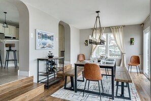 A dining area with a wooden table, chairs, and a chandelier. There is a staircase leading to another level, and a kitchen area is visible in the background. - Lakefront - Pontoon, Hot Tub, Kayaks - Sleeps 12 (Lawton)