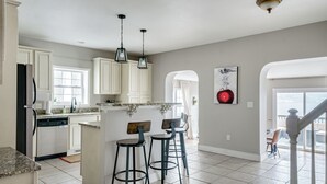 Una cocina con armarios blancos, encimera de granito y dos taburetes de bar. Hay una ventana que ofrece luz natural y vistas al exterior.