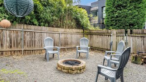 Un jardin avec un foyer en pierre, deux fauteuils Adirondack et une clôture en bois.