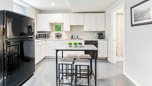 Une cuisine moderne avec des meubles blancs, un réfrigérateur noir, un four à micro-ondes et un coin repas équipé de tabourets.
