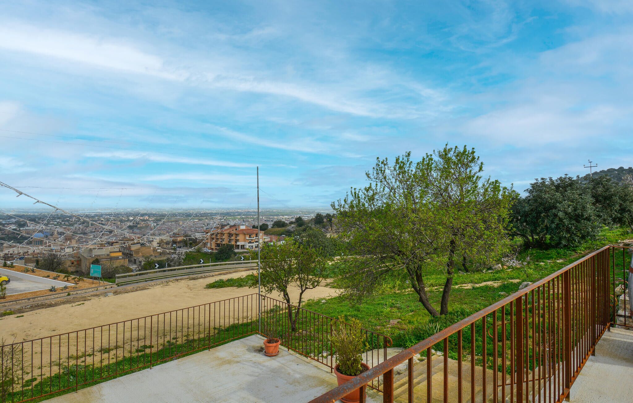 A balcony with a view of a cityscape, a metal railing, and a potted plant.