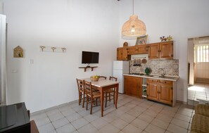 Une cuisine compacte avec des meubles en bois, une table à manger avec des chaises, un téléviseur fixé au mur et un luminaire suspendu.