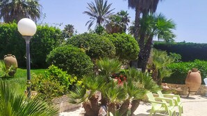 Un jardín con palmeras, un farol y mobiliario exterior.