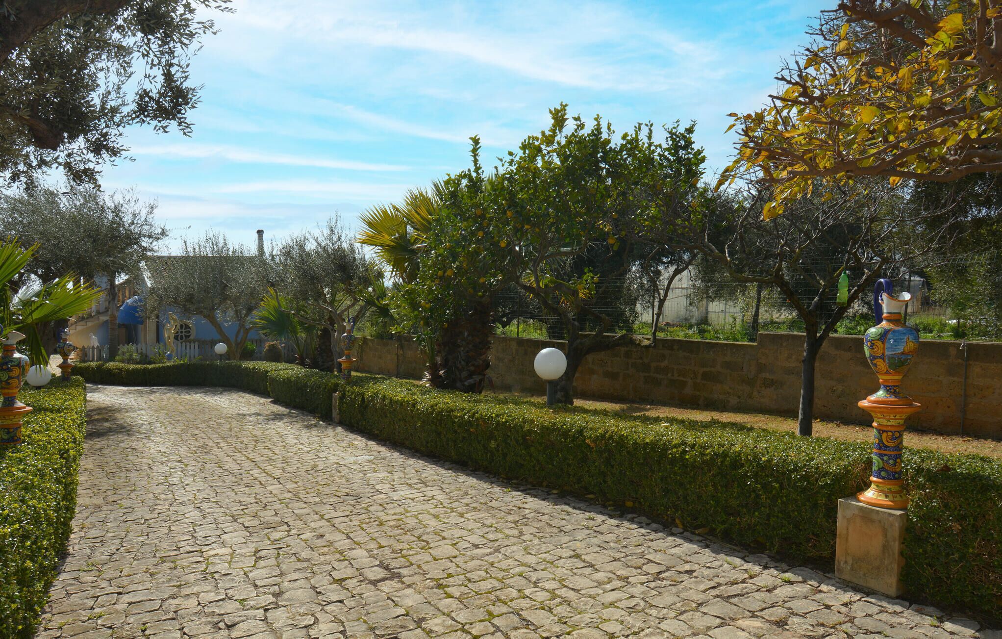 A cobblestone pathway in a garden with neatly trimmed hedges and trees.
