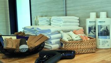 A hotel room with neatly stacked towels, bottles of Ecostore laundry liquid, a basket with toiletries, and a hairdryer on the counter.