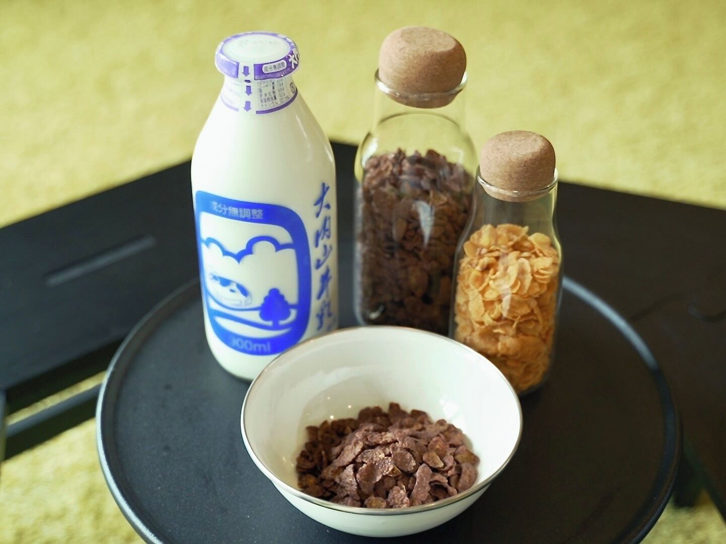 A bottle of milk, two glass containers with brown caps, and a bowl of cereal on a tray.