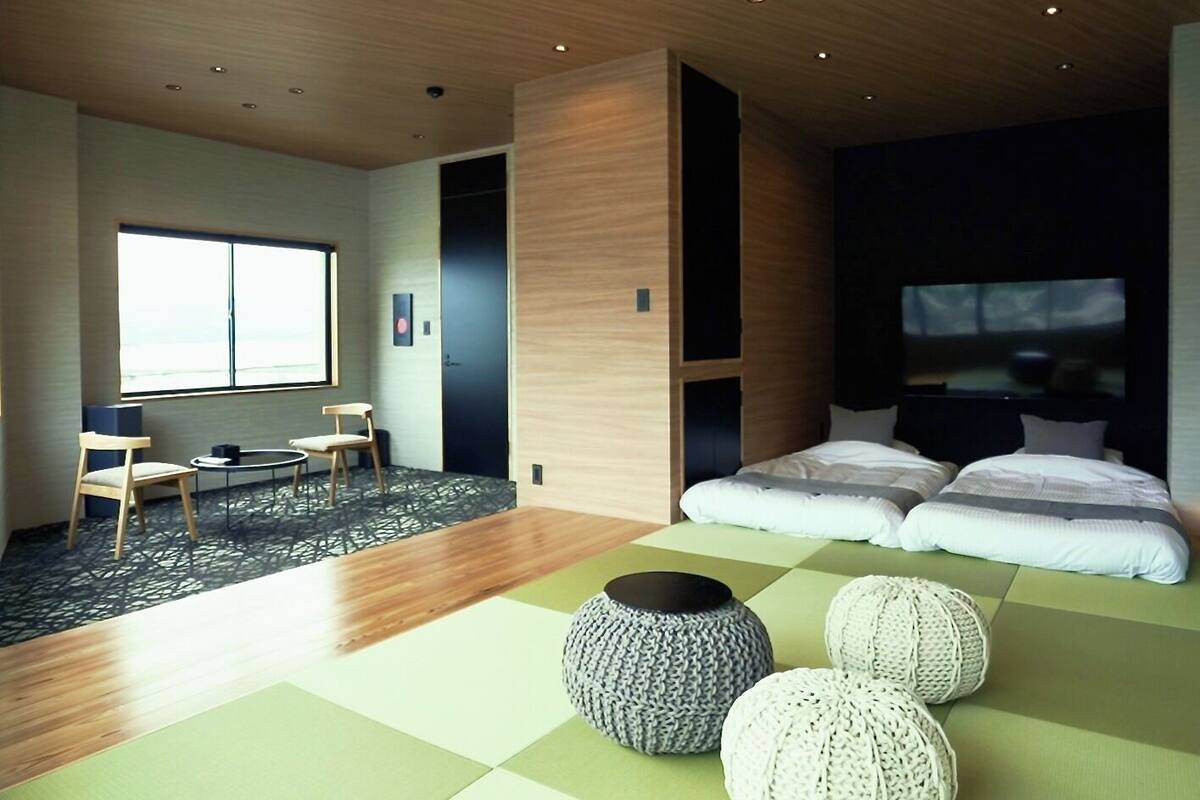 A modern hotel room with a large window, a sofa bed, a small table, and a TV.