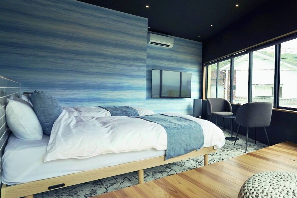 A modern bedroom with a bed, a seating area with chairs, and a large window providing a view.